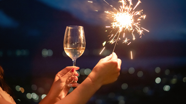 A young woman’s hand holds a glass of champagne and a sparkler.