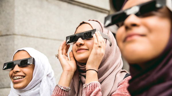 Three young women with eclipse glasses looking at the Sun.