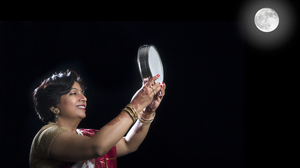 A woman in traditional Indian clothing looking at the Full Moon through a sieve.