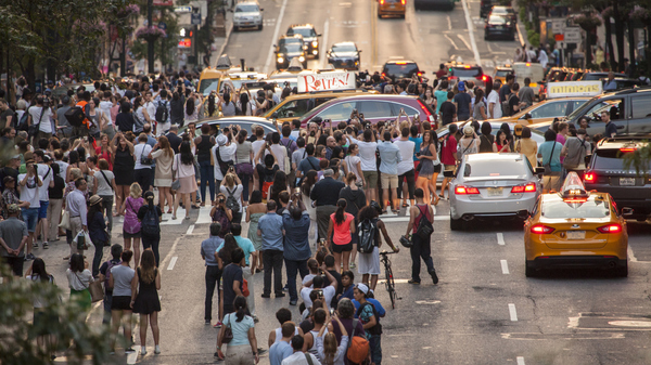 A crowd of people standing on 42nd street in New York, all looking in one direction.