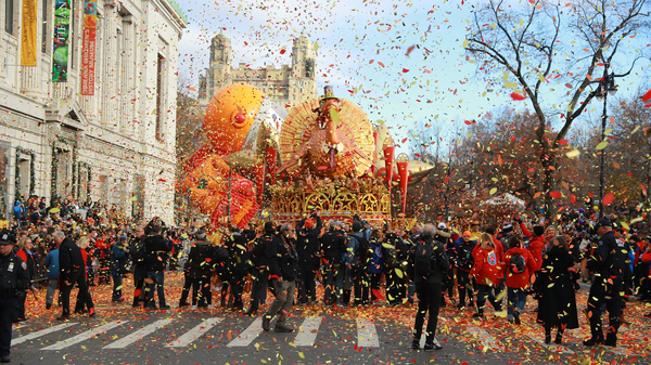 A large turkey float in the Macy's Thanksgiving Day Parade, surrounded by confetti and a crowd of spectators on a city street in New York.