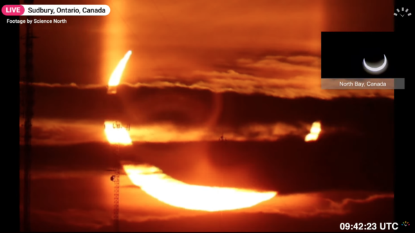 Screenshot from a timeanddate.com live eclipse broadcast showing a partially eclipsed Sun rising in Ontario, Canada. The yellow Sun looks like bright devils horns rising from the horizon.